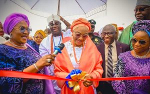 First Lady Senator Oluremi Tinubu, CON, cuts a ribbon during an outdoor commissioning ceremony, flanked by dignitaries including the Ooni of Ife.