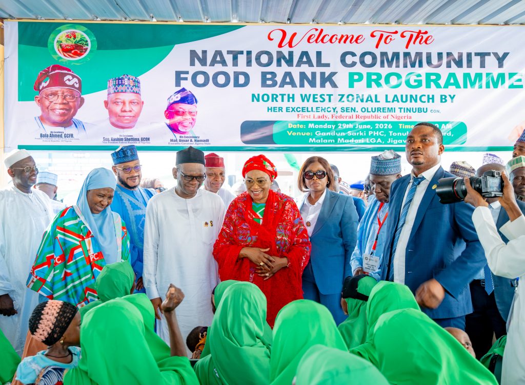 First Lady Senator Oluremi Tinubu, CON, smiling and interacting with children and officials beneath a banner for the National Community Food Bank Programme.