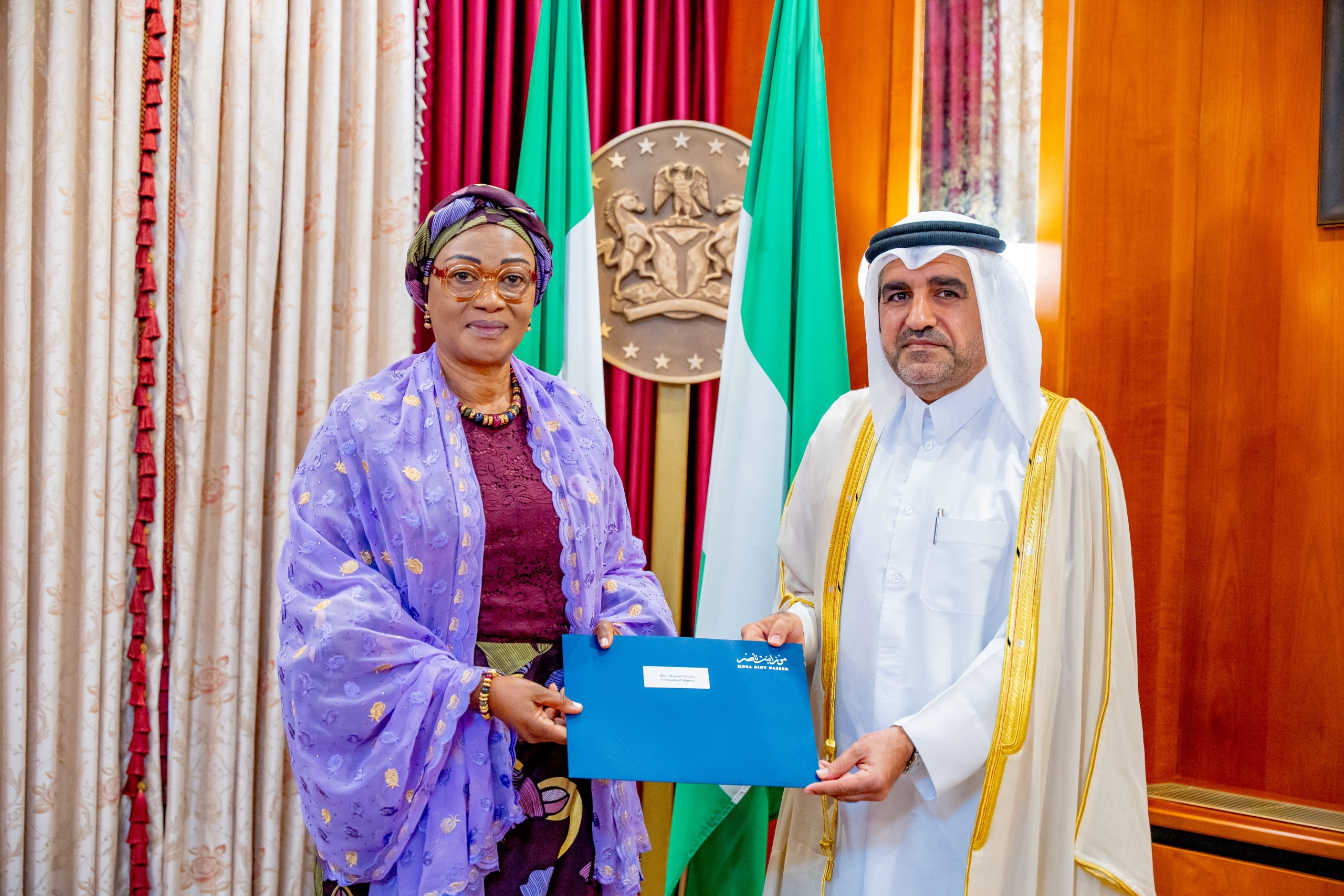 First Lady Senator Oluremi Tinubu, CON, wearing a purple patterned outfit and head wrap, holding a blue folder alongside the Ambassador of Qatar in traditional attire.