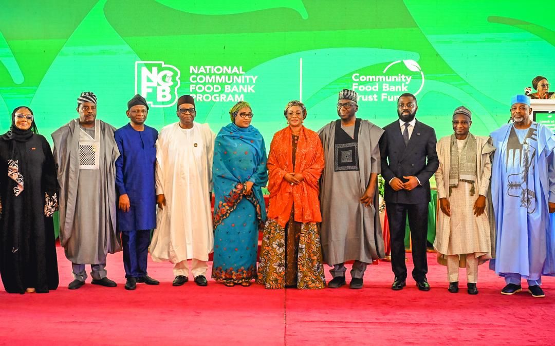 First Lady Senator Oluremi Tinubu, CON, and dignitaries standing in a line on stage in front of a green backdrop for the National Community Food Bank Program.