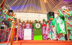 First Lady Senator Oluremi Tinubu, CON, standing behind a green podium bearing the Nigerian coat of arms, surrounded by cheering supporters.