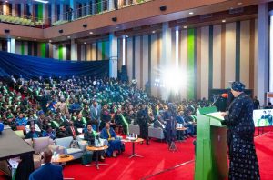 First Lady Senator Oluremi Tinubu, CON, speaking from a podium in front of a large, seated audience inside a grand auditorium.